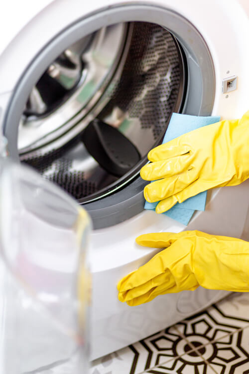 Hand In Protective Glove Carefully Cleaning The Washing Machine. Regular Clean Up. Maid Cleans House.