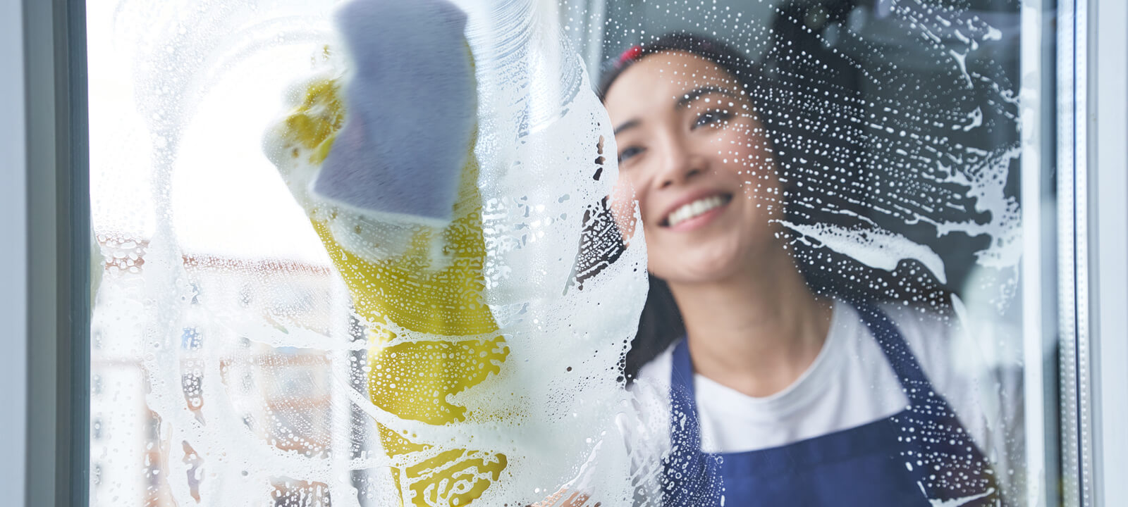 Best Cleaning Service. Cheerful Young Woman Smiling While Cleaning The Window, Glass Surface Using Sponge